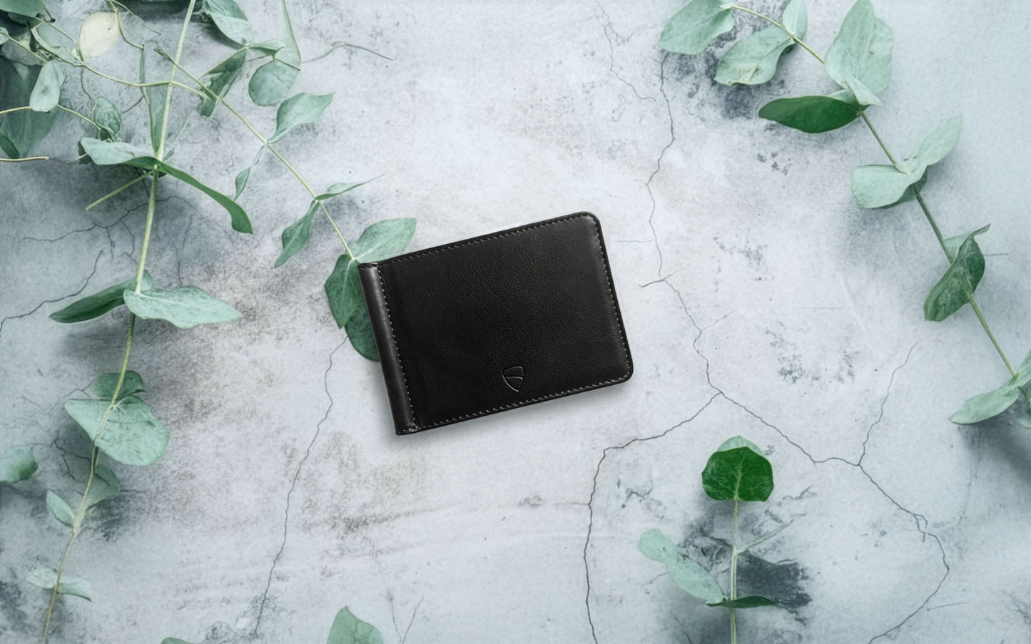 Vaultskin BROMPTON black leather wallet on stone surface with greenery, eco-inspired minimalist wallet with RFID blocking lining